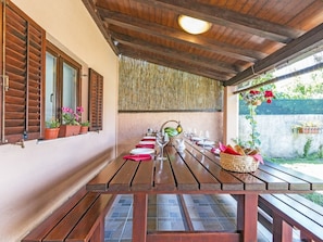 A covered outdoor dining area with wooden benches and tables, potted plants, and a view of greenery. - Heritage House in Orihi With an Elegant Garden (Barban)