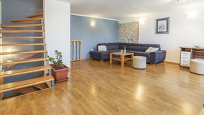 Ein modernes Wohnzimmer mit einer Holztreppe, einem grauen Sofagarnitur, einem Couchtisch und einer Wand mit Steinverkleidung.