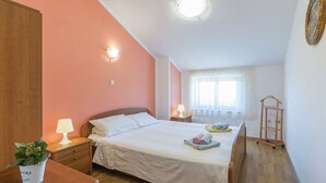 Ein Schlafzimmer mit Bett, Nachttischen, einer Lampe, einem Blumentopf, einem Fenster mit Vorhängen und einer an der Wand stehenden Leiter.