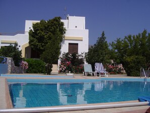 Ein Schwimmbecken mit Liegestühlen und ein Gebäude mit weißer Fassade und einer Tür.