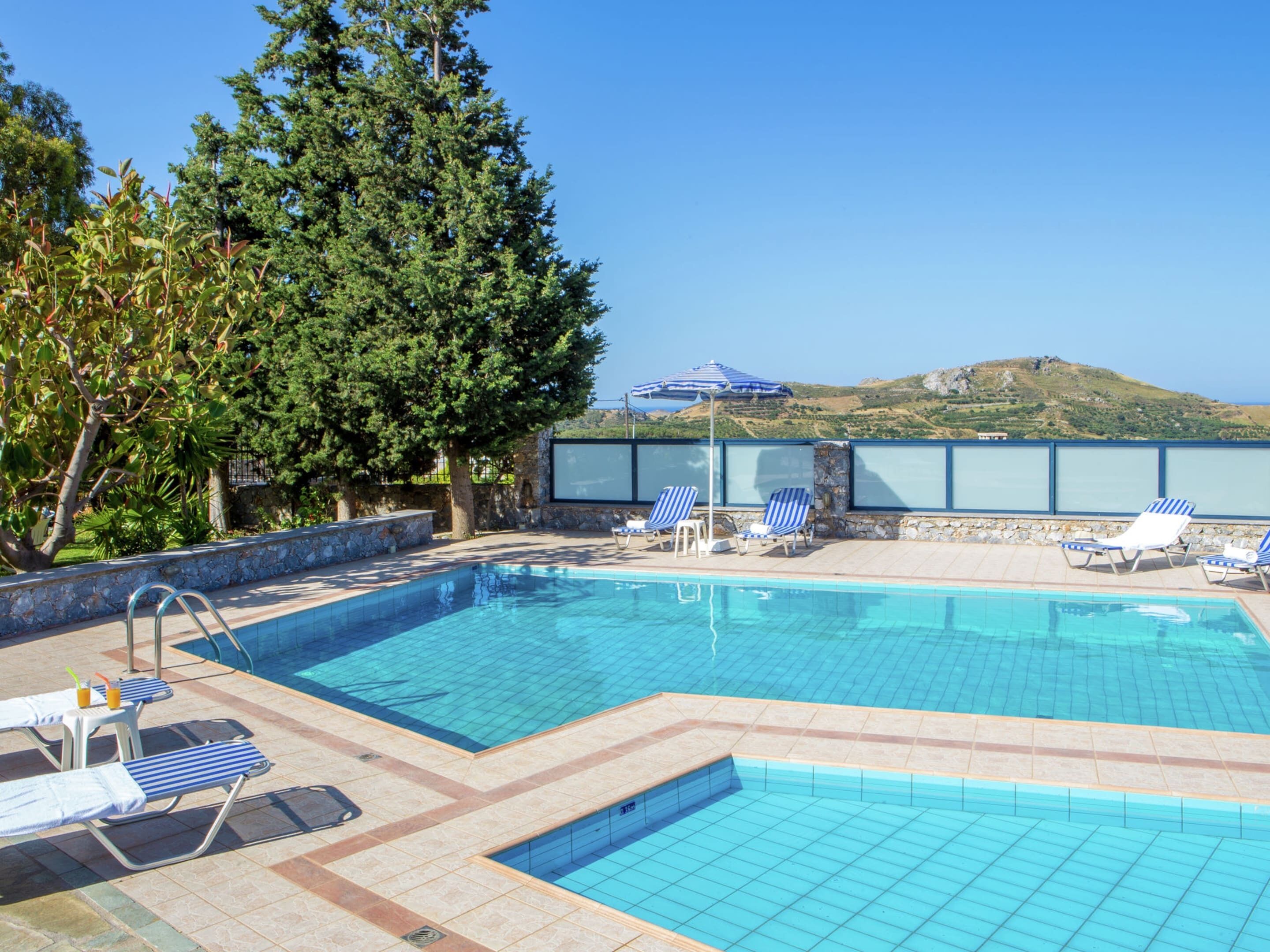 A swimming pool with lounge chairs and a large tree in the background.