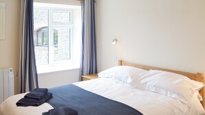 Una cama bien hecha con ropa de cama blanca y azul oscuro, un cabecero de madera y una ventana con cortinas.
