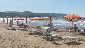 A beach with rows of sun loungers and umbrellas, a clear view of the sea, and a hilly landscape in the background. - Villa Escape Near Orbetello Beach (Orbetello)