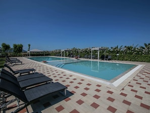 A swimming pool with lounge chairs and umbrellas, surrounded by greenery.