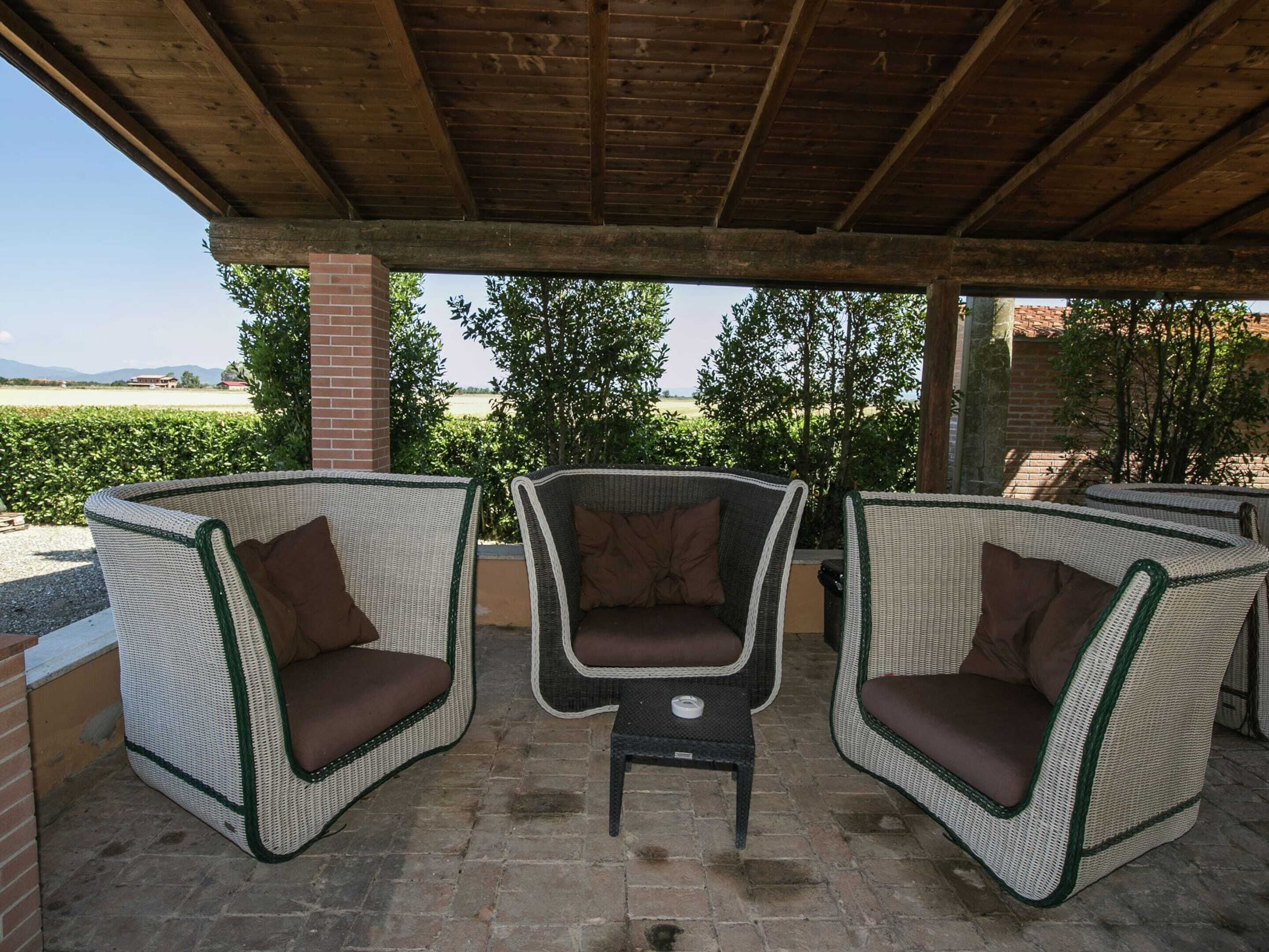 A covered outdoor seating area with wicker chairs and a small table, overlooking a landscaped garden and distant landscape.