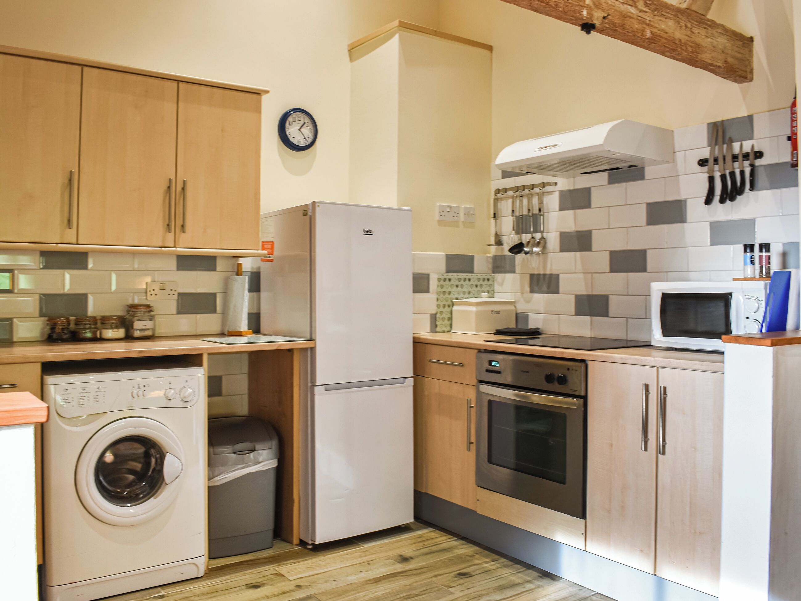 A compact kitchen with wooden cabinets, a washing machine, a refrigerator, a microwave, and an oven.