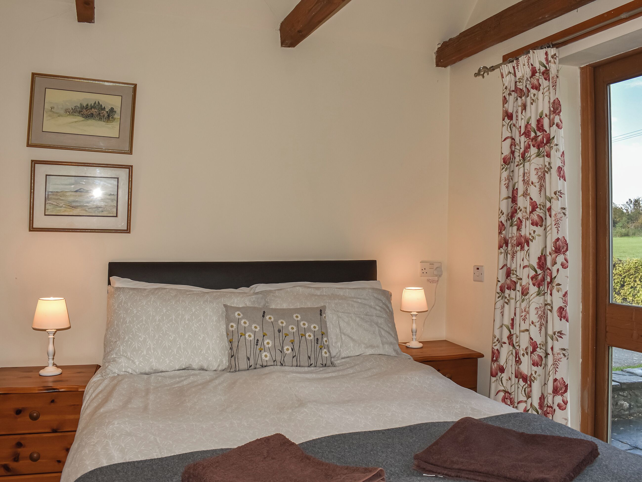 A bedroom with a bed, two bedside lamps, a nightstand, a wooden dresser, and two framed pictures on the wall.