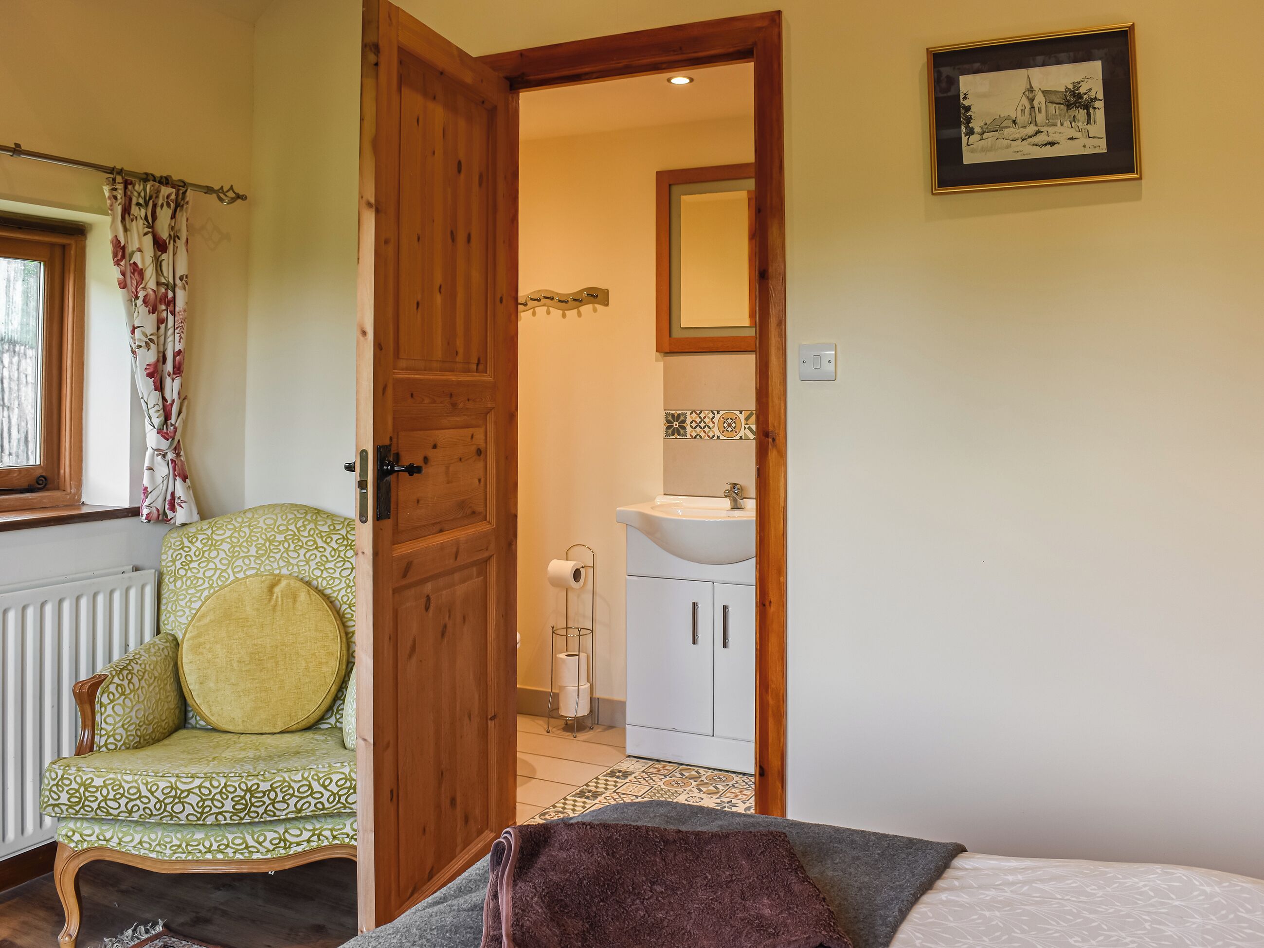 Une pièce avec une porte en bois, une chaise à motifs verts, un lavabo blanc et un tableau encadré accroché au mur.
