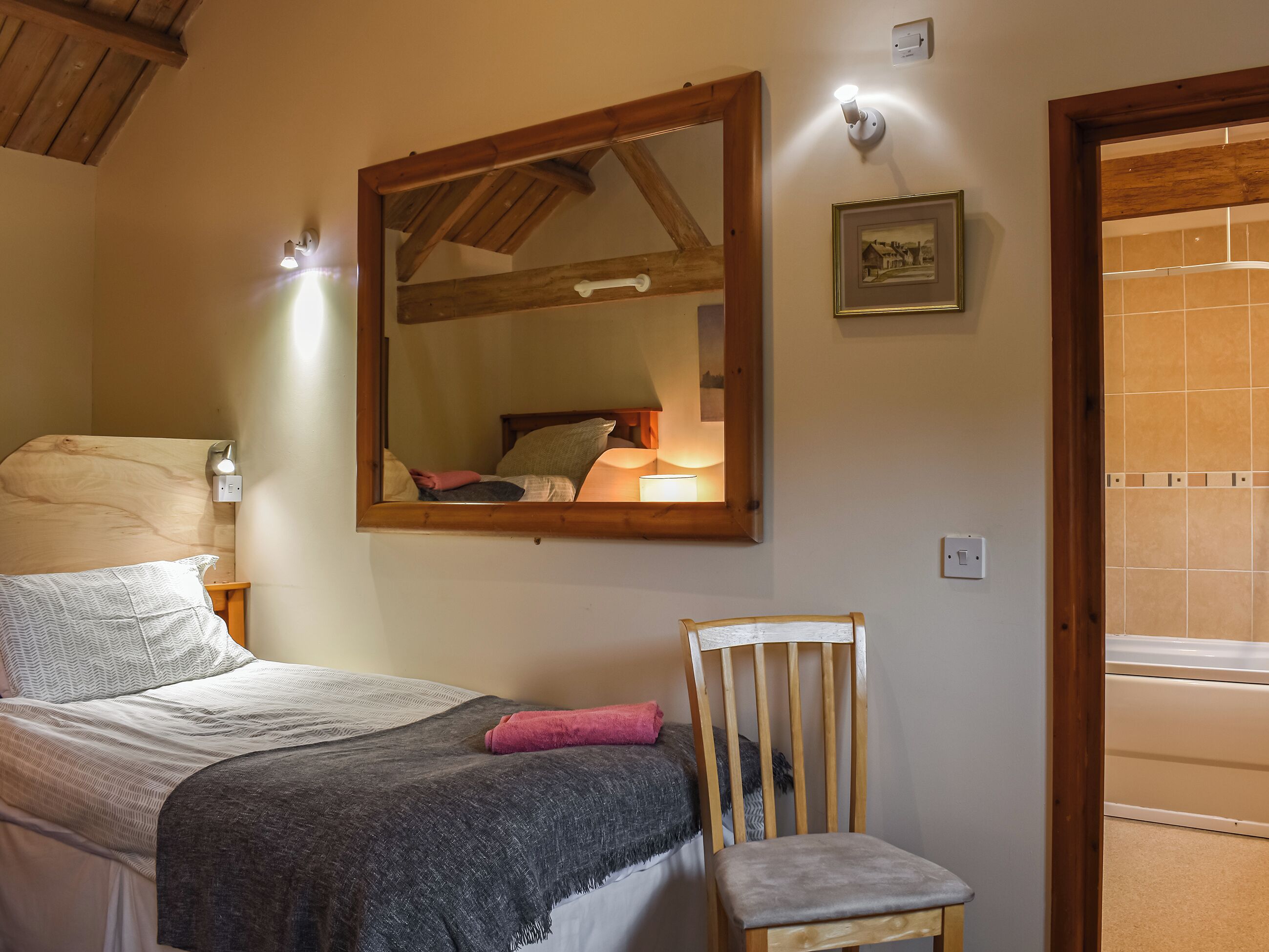 Een slaapkamer met een bed, een stoel, een spiegel en een schilderij aan de muur.