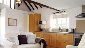 A living room with a sofa, a coffee table with a basket of oranges, and a kitchen area with wooden cabinets, a microwave, and a toaster. - Snug, traditional and romantic perfect for that weekend getaway. (Icklesham)