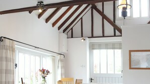 A cozy room with a wooden ceiling, a dining table with chairs, a sofa, and a window with curtains. - Snug, traditional and romantic perfect for that weekend getaway. (Icklesham)