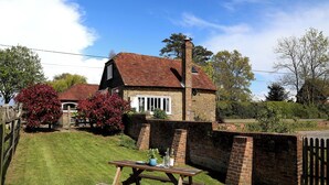 A traditional brick house with a red-tiled roof and a chimney, surrounded by a well-maintained lawn and a wooden fence. - Snug, traditional and romantic perfect for that weekend getaway. (Icklesham)