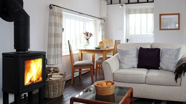A cozy living room with a wood-burning stove, a sofa, a dining table, and a window with curtains. - Snug, traditional and romantic perfect for that weekend getaway. (Icklesham)