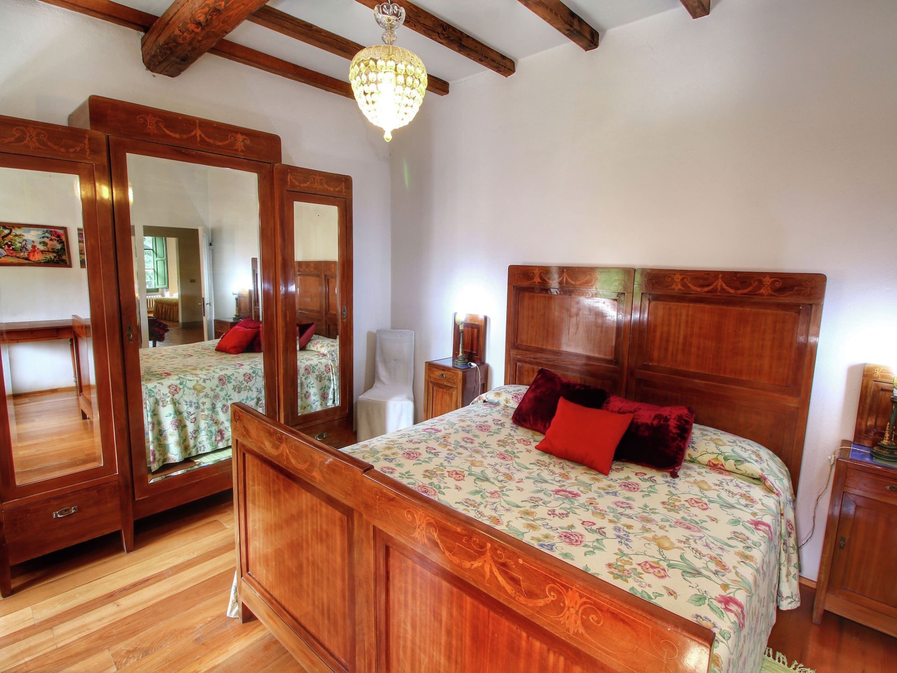 Ein Schlafzimmer mit einem hölzernen Bett, einem großen Spiegel und einer Kronleuchter.