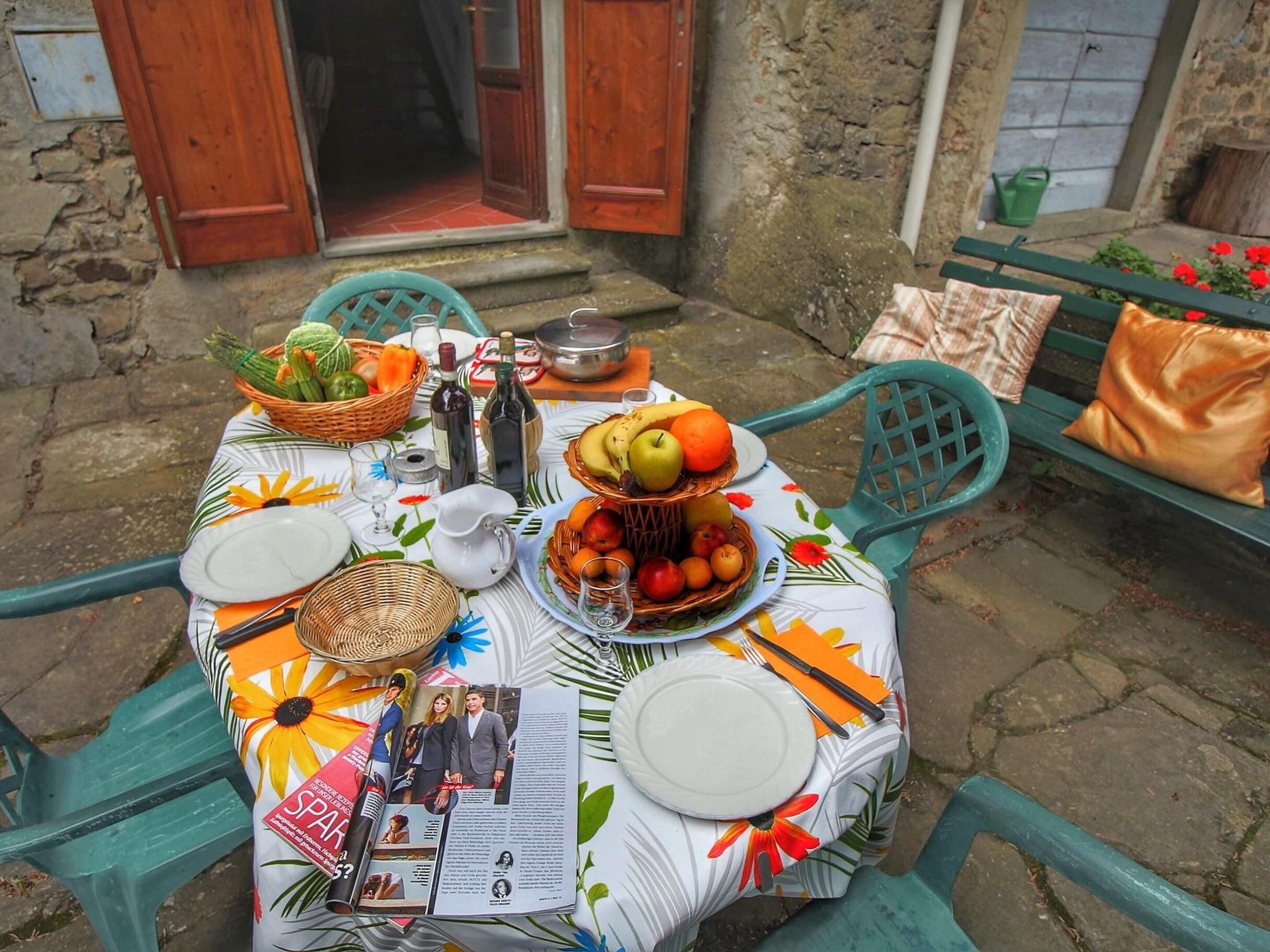 Une table dressée à l’extérieur, avec une variété de fruits, des bouteilles et un magazine.