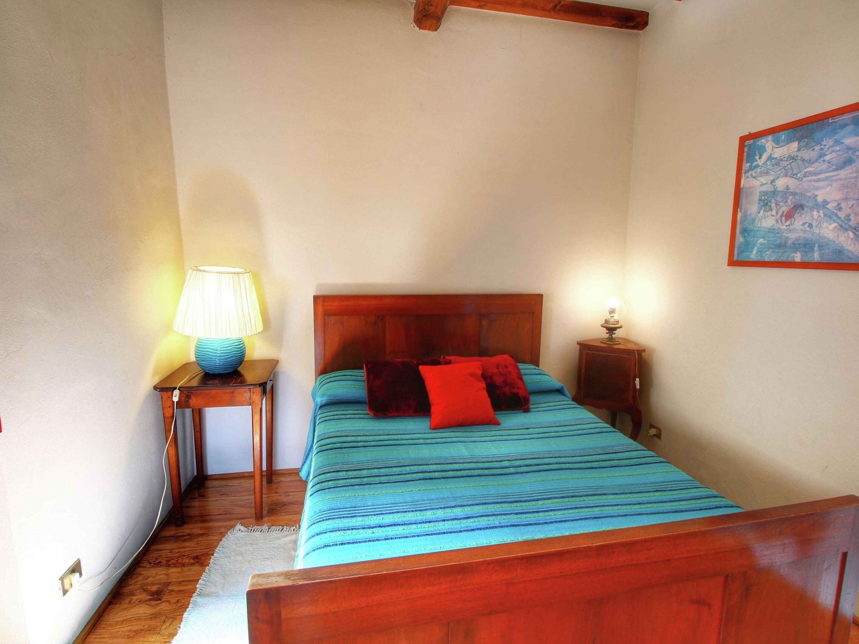 Une chambre à coucher avec un lit en bois, une table de chevet avec une lampe et un tableau accroché au mur.