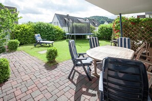A patio with a round table and chairs, a trampoline, and a covered seating area.