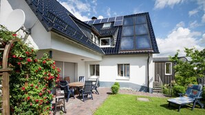 Ein Haus mit geneigtem Dach, Solaranlagen, einer Terrasse mit Tisch und Stühlen und einem gepflegten Rasen.