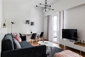 A modern living room with a sofa, a dining table with chairs, a TV, and a large window.