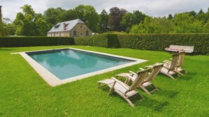 Ein rechteckiger Swimmingpool mit einer Holzterrasse und Liegestühlen in einem gepflegten Rasenbereich.