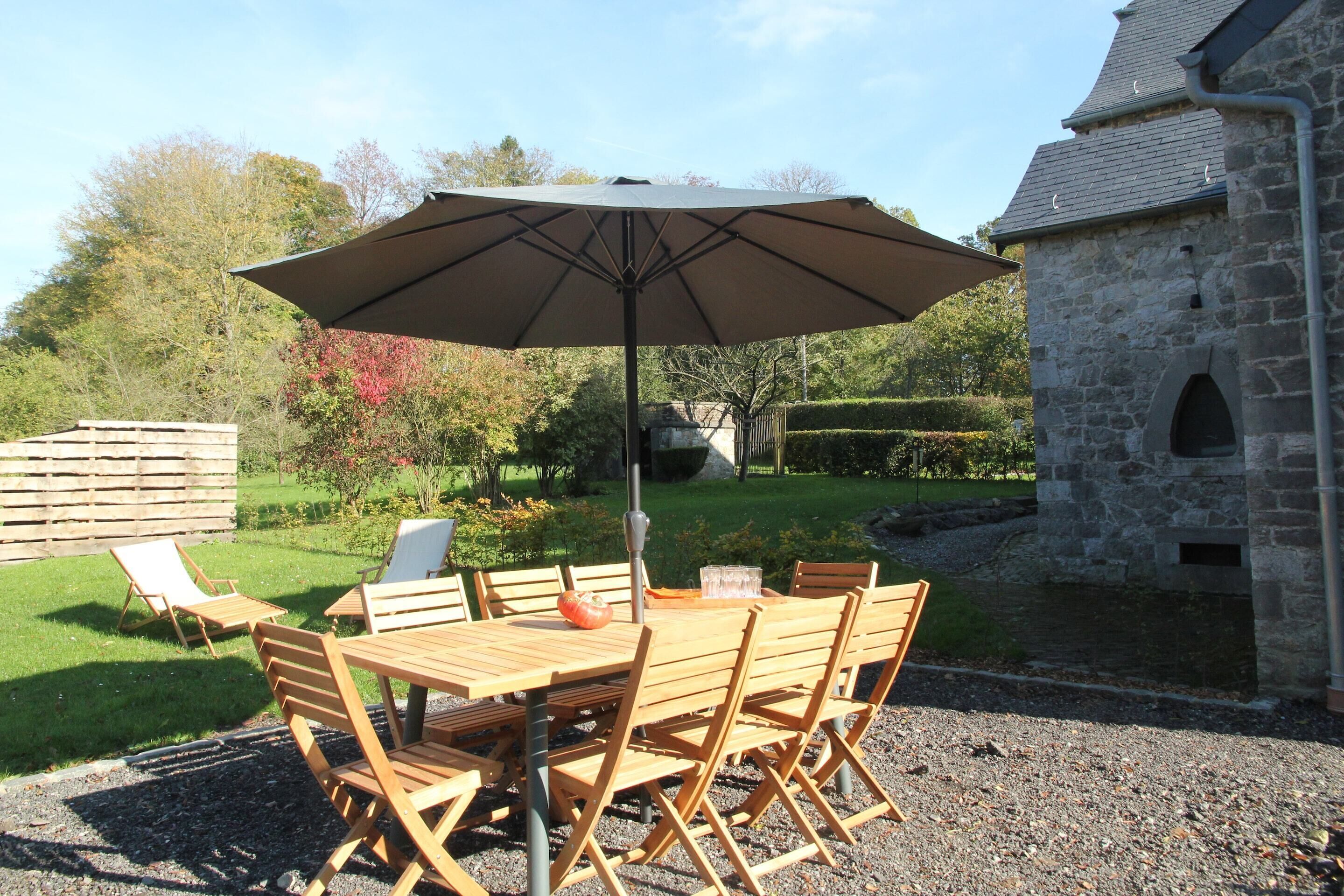 An outdoor patio with a wooden table and chairs, a large umbrella, and a stone building in the background.