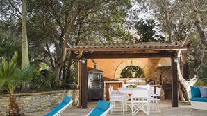 Un patio exterior con sillones de descanso, una mesa de piedra y zona de barbacoa.