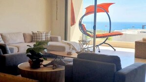 A modern living room with a sofa, armchairs, a coffee table, and a view of the ocean through large windows. - OCEAN VIEW AMAZING CONDO@VISTAVELA4104 (Cabo San Lucas)