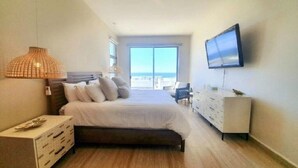 A bedroom with a bed, a dresser, a TV, and a large window. - OCEAN VIEW AMAZING CONDO@VISTAVELA4104 (Cabo San Lucas)