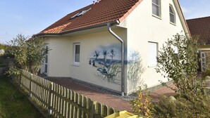 A two-story house with a red-tiled roof, a small garden, and a wooden fence. - Ferienhaus mit Sauna in Boiensdorf am Salzhaff (Boiensdorf)