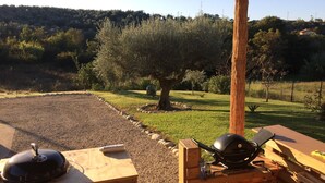 A wooden deck with a grill and barbecue tools, surrounded by a gravel area and a grassy field with trees. - Holiday Home Picciano Near Medieval Towns (Picciano)