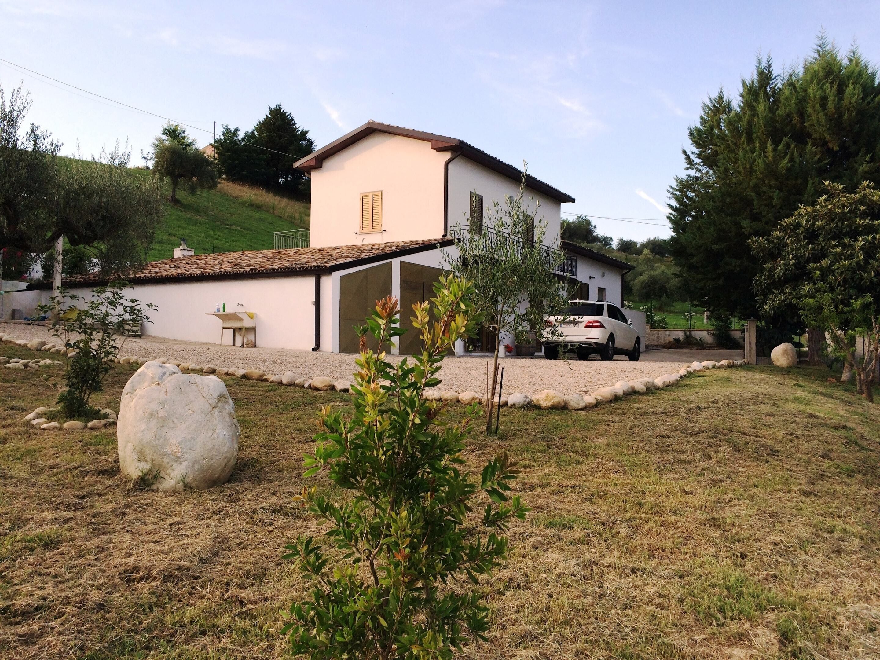 A house with a garage, a driveway, and a lawn with a large rock and a small tree.