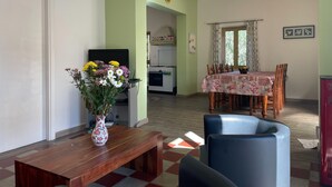 A living room with a wooden coffee table, a vase of flowers, and a dining area with a table set for four. - Holiday Home Picciano Near Medieval Towns (Picciano)