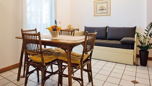 A dining area with a table, chairs, and a fruit basket. There is a sofa and a potted plant in the background. - Belvilla by OYO Catalani Bilo (Riccione)