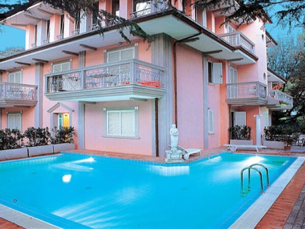 Un immeuble à plusieurs étages doté d’une piscine, de balcons et d’une statue au centre.