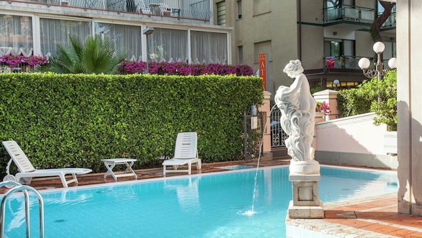 A swimming pool with lounge chairs, a statue, and a hedge. - Belvilla by OYO Catalani Bilo (Riccione)