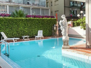 Une piscine avec des chaises longues, une statue et une haie.