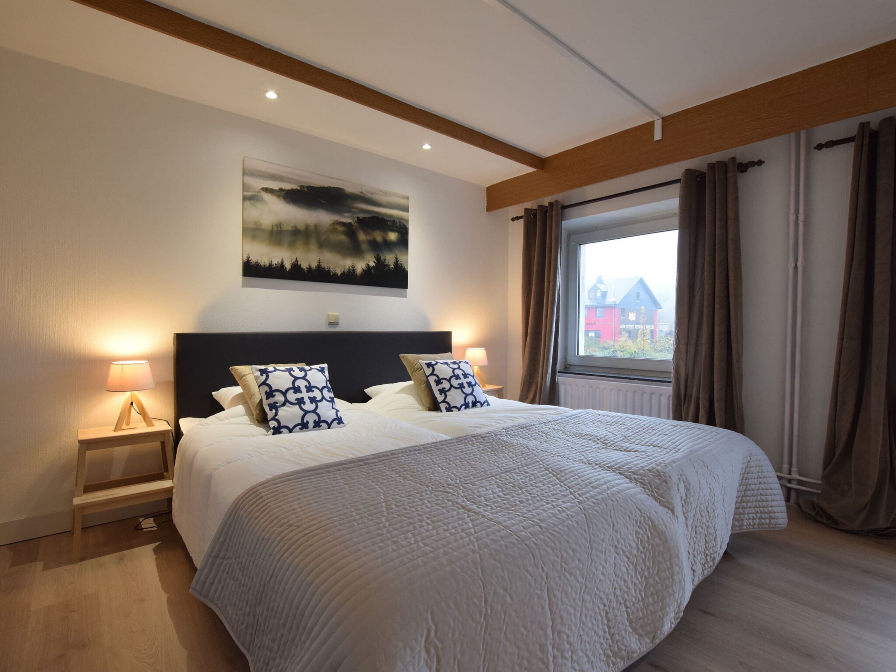 Quarto com uma cama grande, duas mesas de cabeceira com abajures, um quadro sobre a cama e uma janela com cortinas.