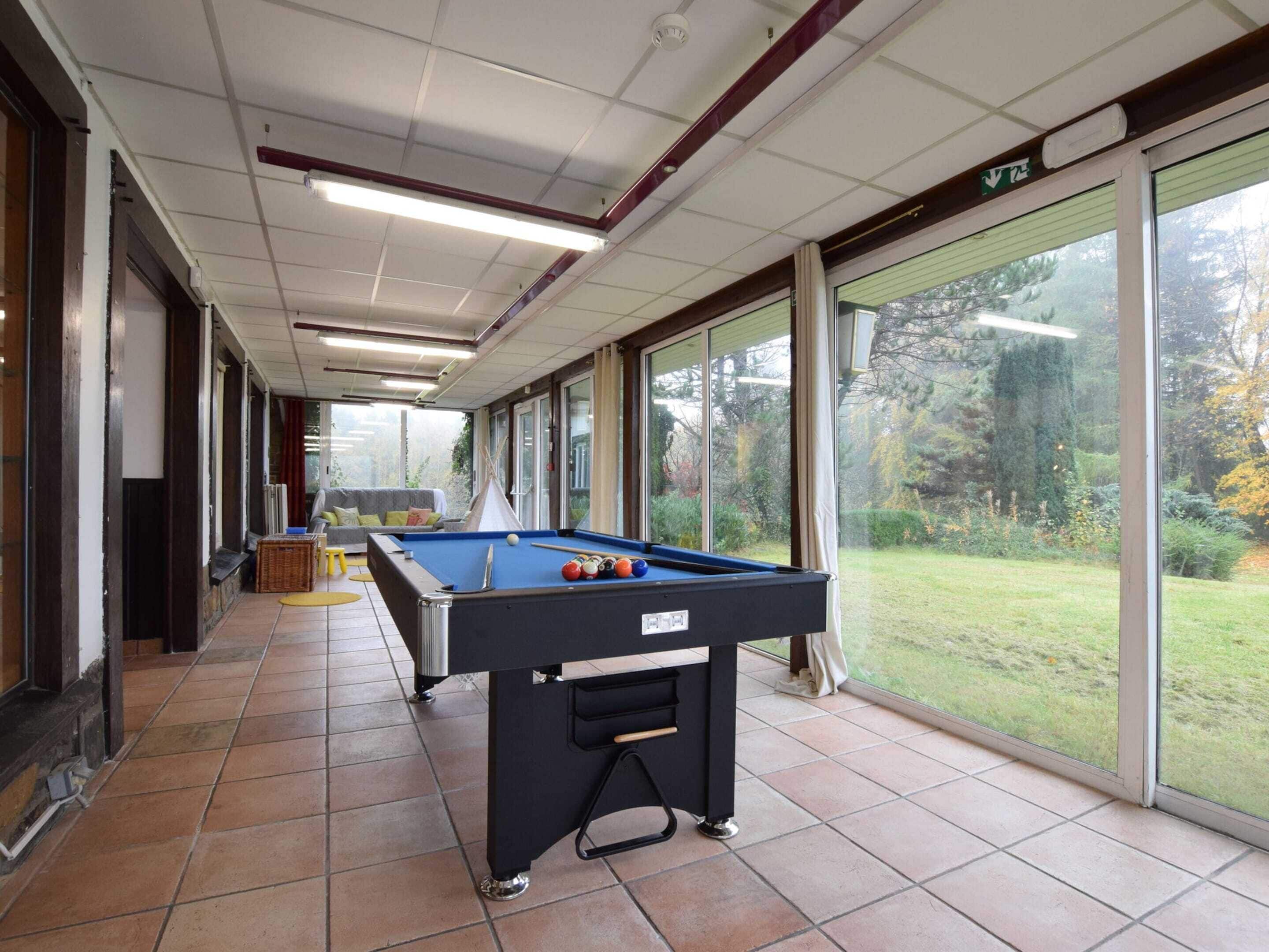 A pool table in a room with large windows and a view of a garden.