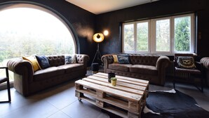 Un salon avec deux canapés en cuir, une table basse en bois et une grande fenêtre donnant sur la forêt.