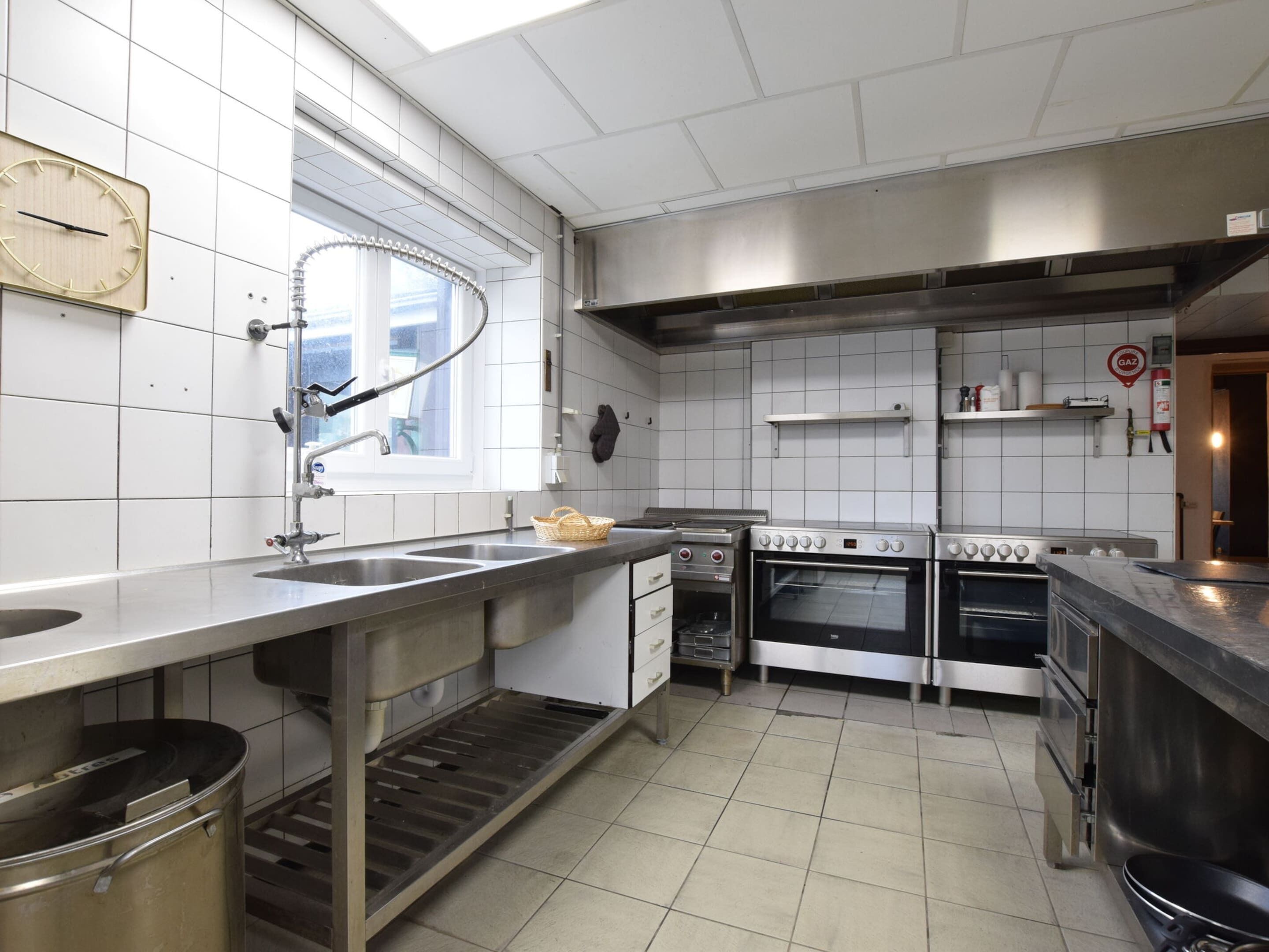 Cozinha comercial com eletrodomésticos de aço inoxidável, uma janela e paredes revestidas de azulejos.