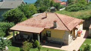 A small stone house with a tiled roof, a covered patio, and a view of a lake. - Rural house Pontevedra. Pool, garden and barbecue (Vilaboa)
