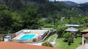 A swimming pool with lounge chairs, a stone wall, and a view of a forested hillside. - Rural house Pontevedra. Pool, garden and barbecue (Vilaboa)