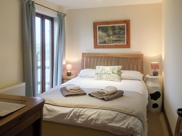 A neatly made bed with a headboard, two bedside lamps, and a window with curtains. - The Coach House - 15661 (East Tytherton, Chippenham)