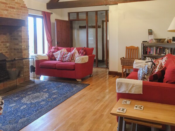 A living room with a red sofa, a wooden coffee table, a fireplace, and a bookshelf. - The Coach House - 15661 (East Tytherton, Chippenham)