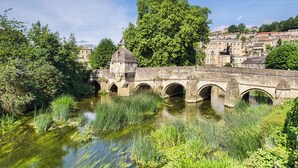 A stone bridge with multiple arches over a river, surrounded by greenery and historic buildings in the background. - The Coach House - 15661 (East Tytherton, Chippenham)