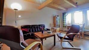 Ein Wohnzimmer mit Holzboden, einem schwarzen Ledersofa, einem Couchtisch aus Holz und einem Schaukelstuhl.