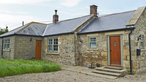 A stone building with a sloped roof, two wooden doors, and a small front porch with steps. - 2 bedroom accommodation in Alnham, near Rothbury (Alnham, near Rothbury)