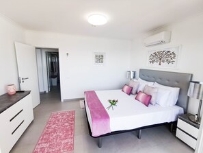 Une chambre à coucher comprenant un lit, des tables de chevet, une commode, un bureau, une chaise, une porte et un couloir.