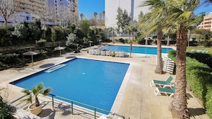 A pool area with a rectangular pool, lounge chairs, palm trees, and a stone pathway. - Flat Rose Garden Sea View (Portimão)