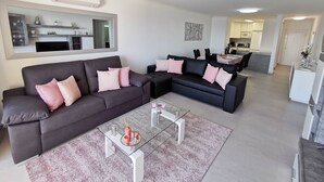 A modern living room with two dark sofas, a glass coffee table, and a kitchen in the background. - Flat Rose Garden Sea View (Portimão)